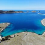 An aerial photograph of Bijela Lučica, a stunning turquoise bay in National Park Kornati. The crystal blue water shines bright against the rugged rocky terrain of the surrounding islands. Little White Port - Kornati Islands Accommodation.