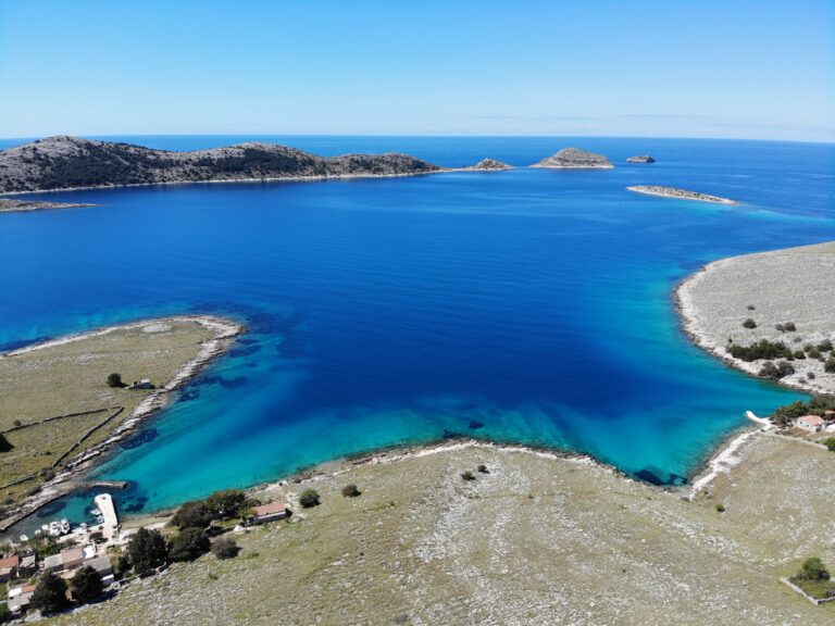 An aerial photograph of Bijela Lučica, a stunning turquoise bay in National Park Kornati. The crystal blue water shines bright against the rugged rocky terrain of the surrounding islands. Little White Port - Kornati Islands Accommodation.